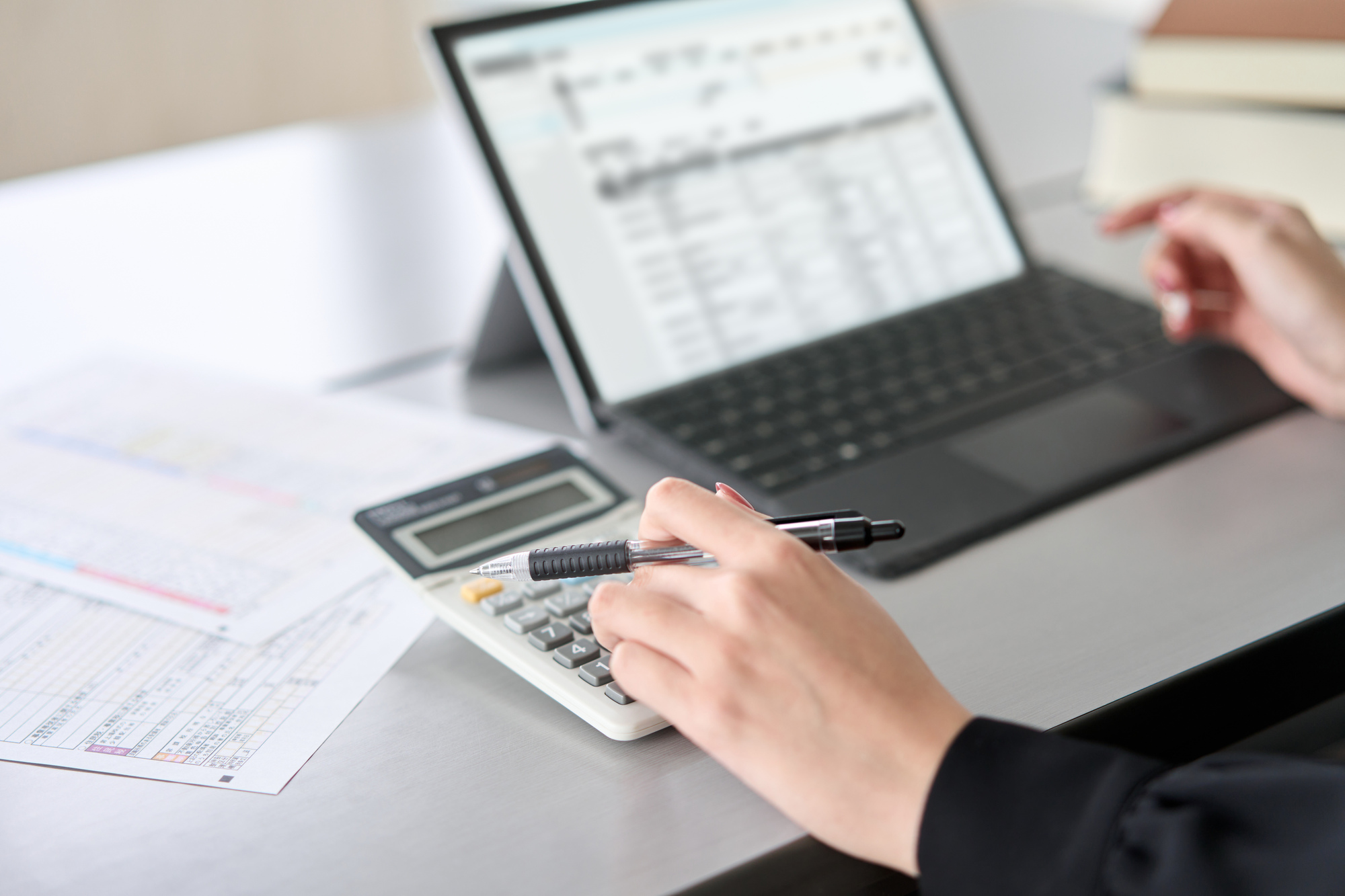 Payroll administrator reviewing calculations with a laptop and calculator
